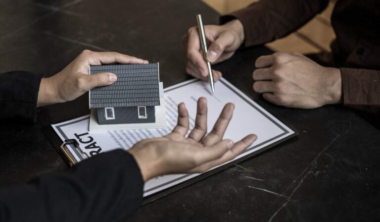 Dos personas sosteniendo un modelo de casa sobre una mesa.