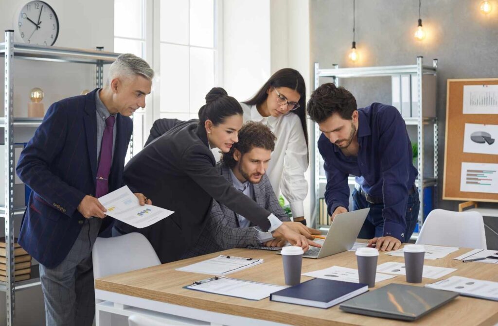 Airbnb vs Home Vacation Group Un grupo de profesionales colaborando en un proyecto frente a un laptop en un entorno de oficina.