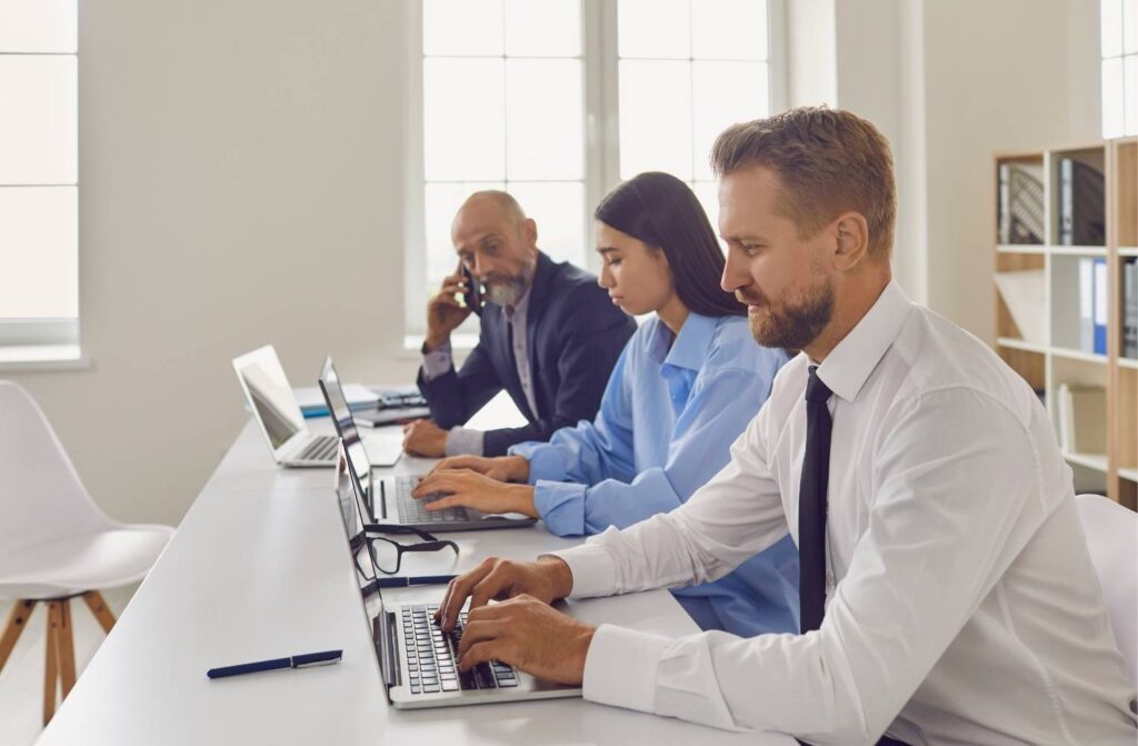 Tres personas trabajando en laptops en una oficina moderna, colaborando en un proyecto.
