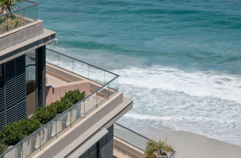 Balcón con vista al océano y la playa, mostrando un paisaje sereno y soleado.