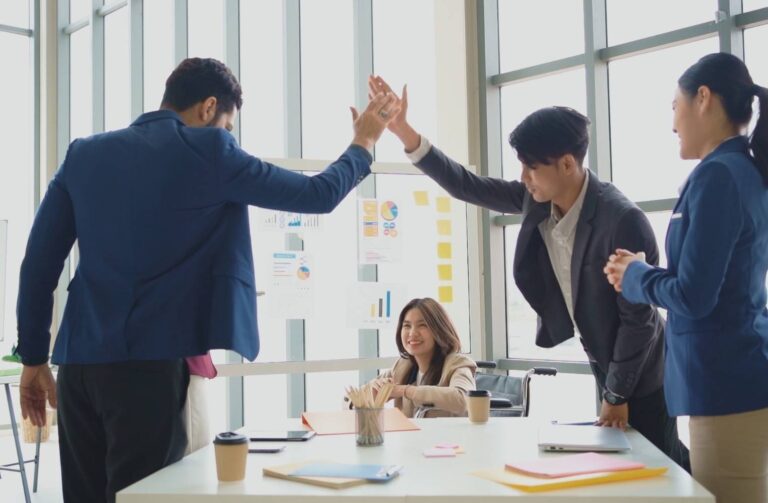 Personas de negocios en una oficina dándose un choque de manos en señal de celebración.