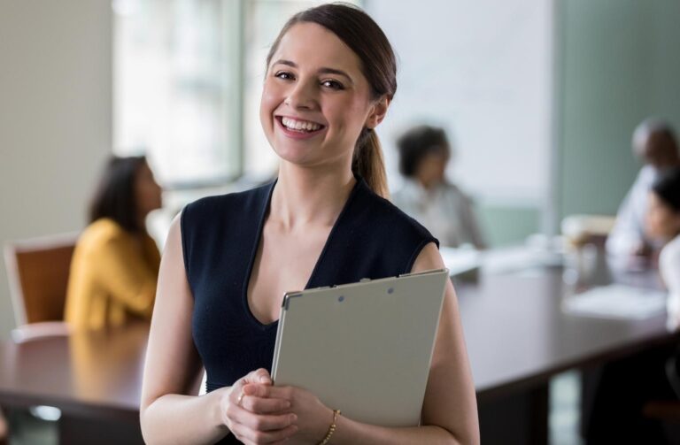 Mujer sonriente sosteniendo una carpeta, mostrando una actitud positiva y amigable.