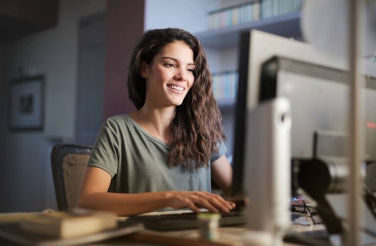 caso de exito Mujer feliz frente a su computadora, disfrutando de su trabajo mientras sonríe.