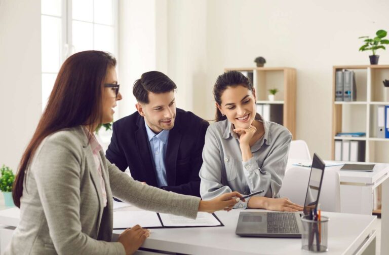 property management Tres profesionales de negocios sentados a una mesa con un portátil abierto entre ellos.