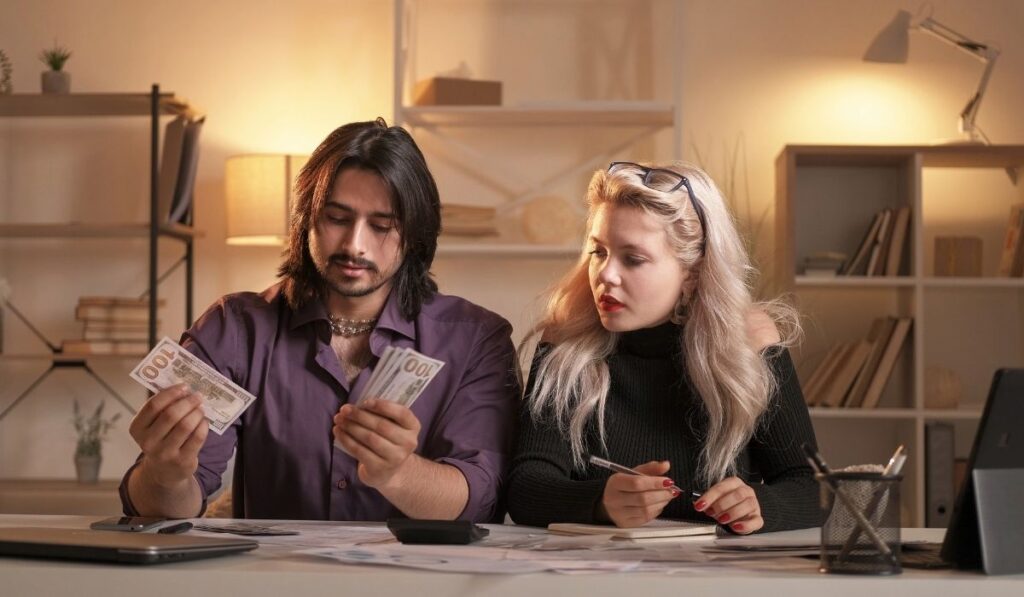 Pareja sentada en una mesa, con dinero frente a ellos, ajustando los gastos