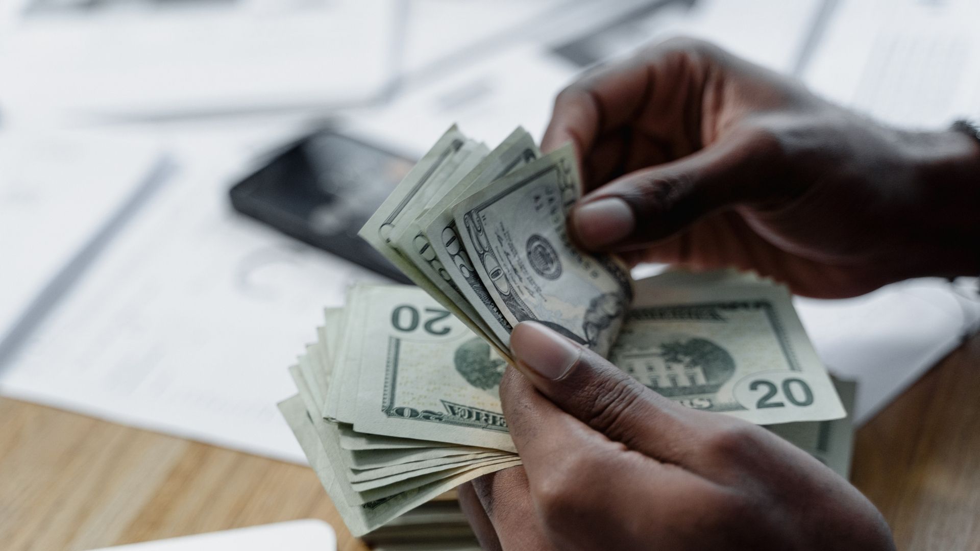 Persona sosteniendo un fajo de dinero sobre un escritorio, simbolizando el crecimiento de ingresos