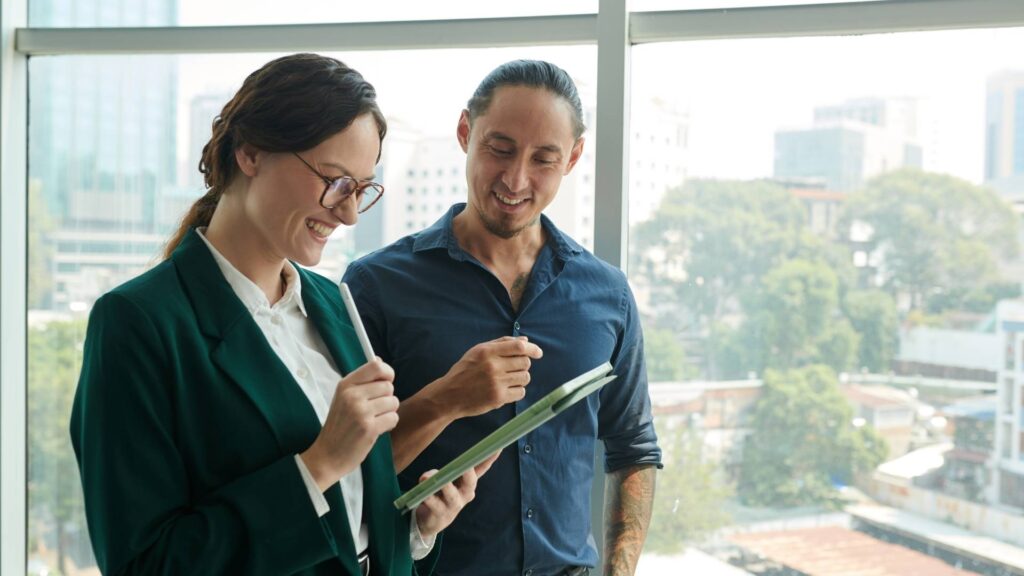 Dos profesionales de negocios frente a una ventana, revisando una tablet juntos en la oficina de Home Vacation Group