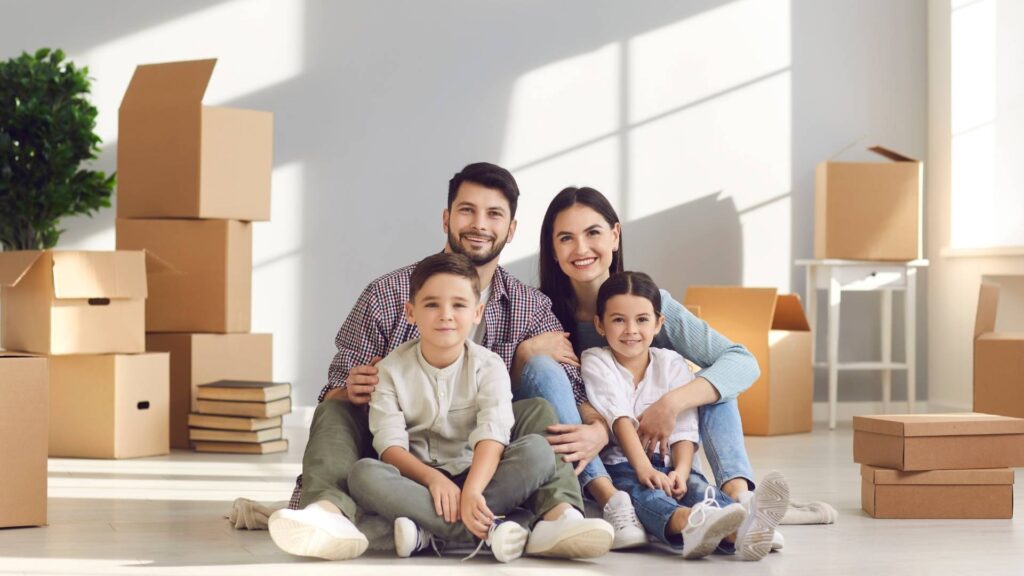 Una familia sentada en el suelo de una habitación vacía rodeada de cajas, disfrutando de su tiempo juntos