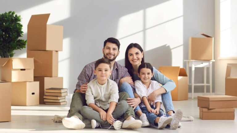Una familia sentada en el suelo de una habitación vacía rodeada de cajas, disfrutando de su tiempo juntos