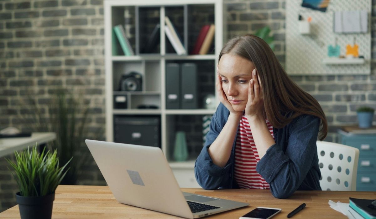A woman at a desk, head in hands, reflecting on the challenges of self-management and its appealing illusion