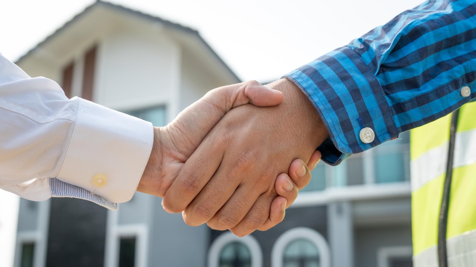 Two people shaking hands in front of a house, symbolizing collaboration in property management in Orlando.