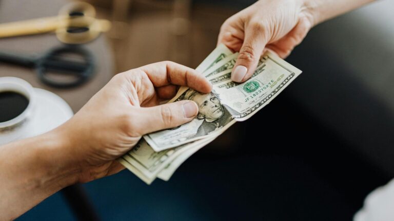 Persona entregando dinero en dólares a otra persona.