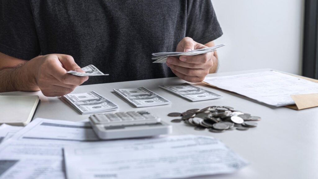  Un hombre cuenta dinero sobre una mesa, rodeado de un montón de billetes.