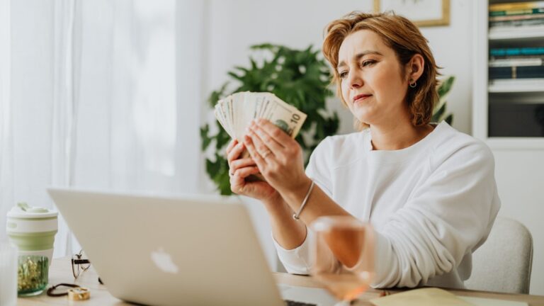 Mujer sentada en un escritorio sosteniendo dinero, en el contexto de una casa vacacional.