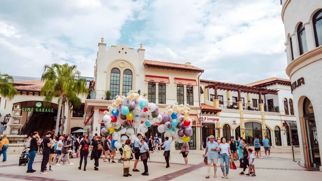 Personas caminando por un centro comercial, sosteniendo globos coloridos durante un día de vacaciones.