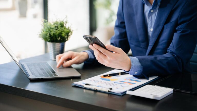 Empresario sentado en su escritorio, usando su smartphone, simbolizando una buena administración en su trabajo diario.
