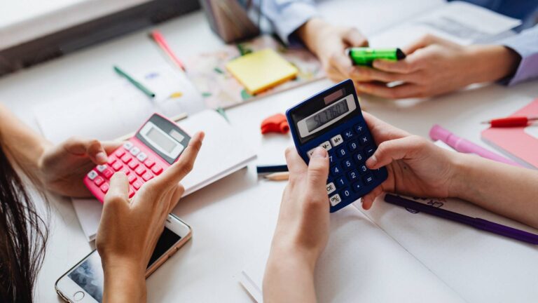 Varias personas utilizando calculadoras y smartphones en una mesa con notas para calcular la rentabilidad real de una casa vacacional.