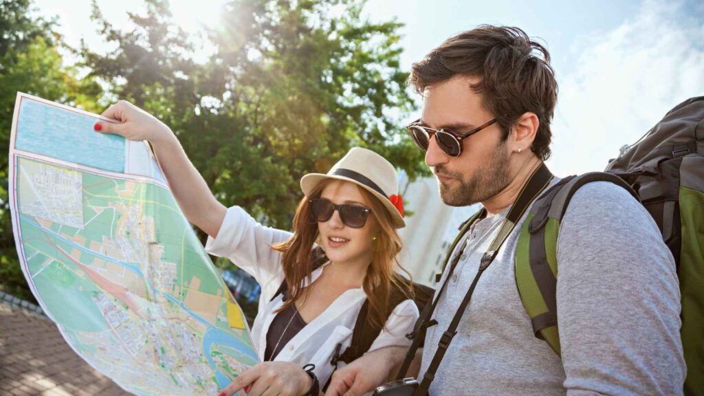 Pareja de turistas con mochilas consultando un mapa de la ciudad de Orlando para planificar su visita a los parques temáticos.