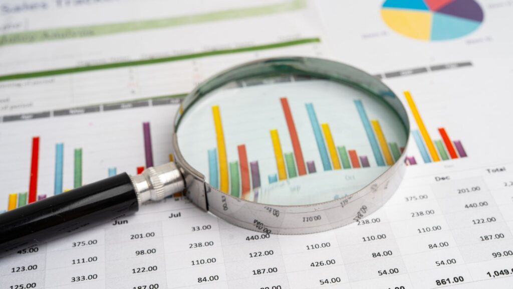 Lupa sobre gráficos financieros analizando datos para calcular el retorno de inversión real en proyectos inmobiliarios.