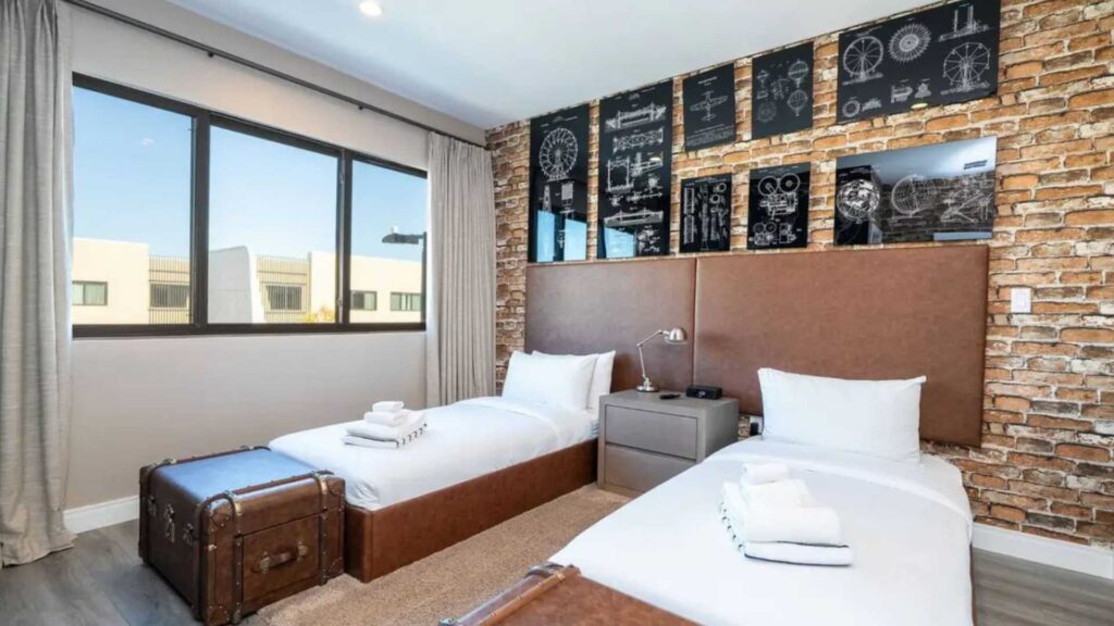 Habitación moderna con camas gemelas y pared de ladrillo, preparada para la gestión de alquileres cortos profesional.