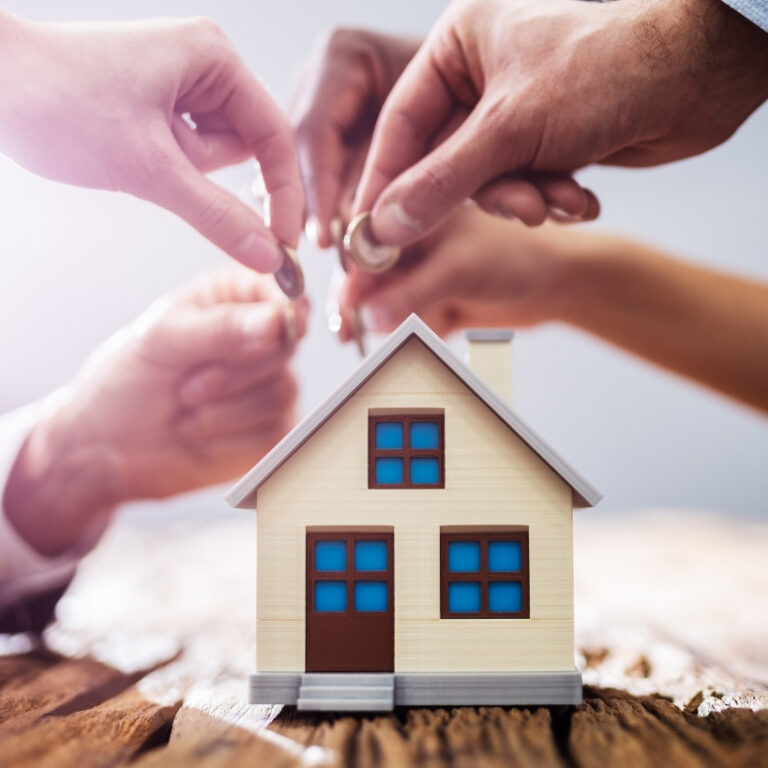 Orlando 2026 Varias manos depositando monedas en una casa de juguete, simbolizando el ahorro para una inversión inmobiliaria en Orlando 2026.
