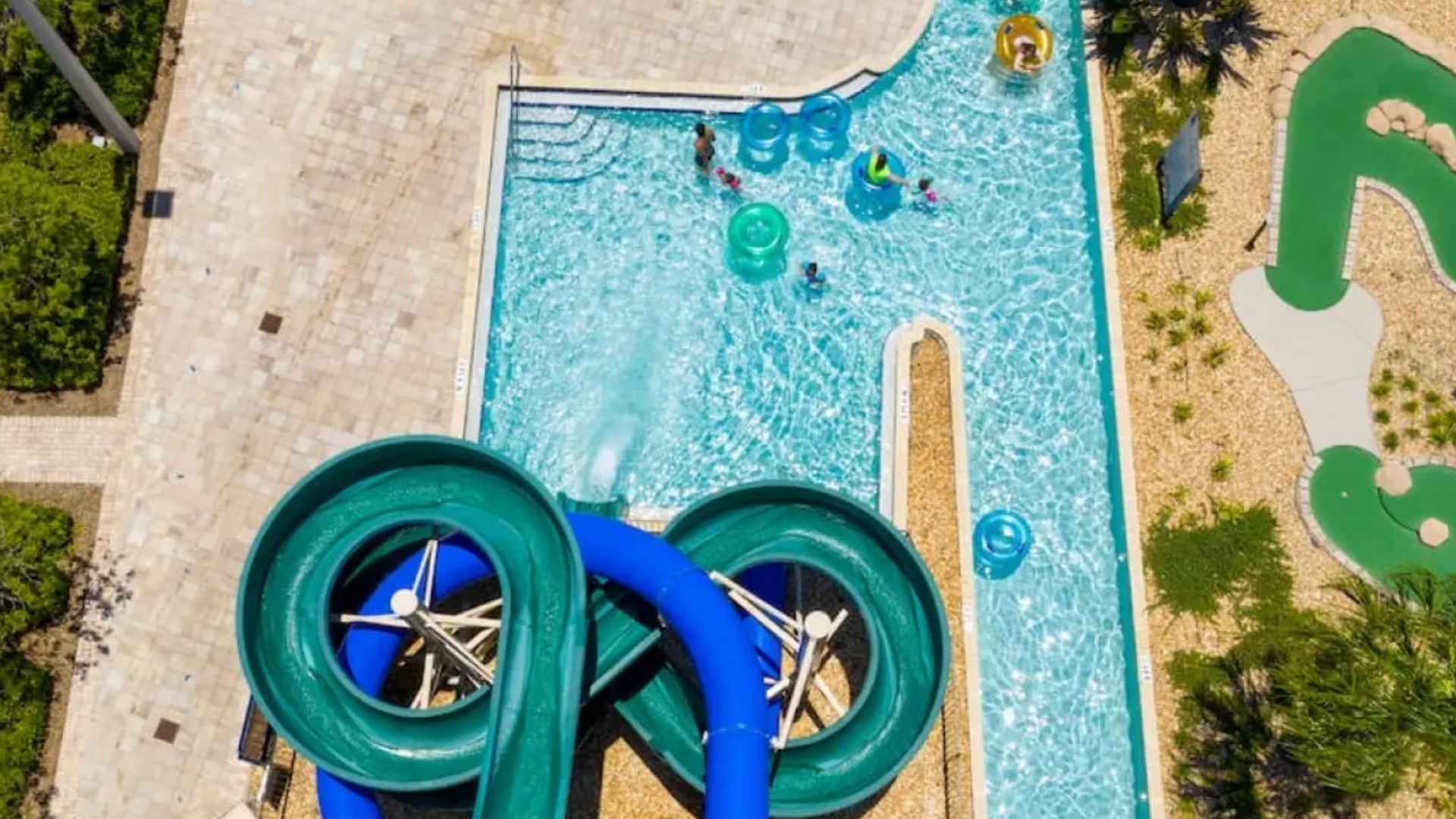 Piscina en Kissimmee tipo resort con toboganes acuáticos, río lento y área de juegos; personas disfrutando flotadores bajo el sol