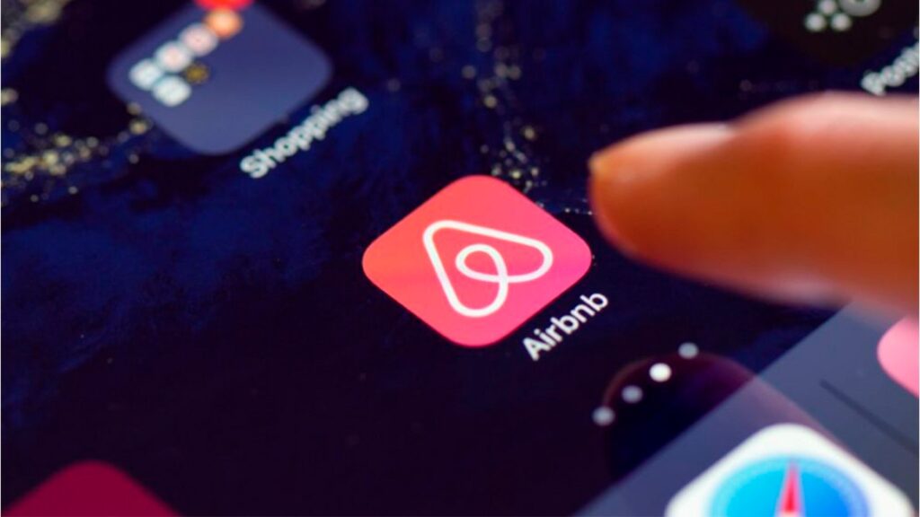 Primer plano de un dedo tocando el icono de la aplicación Airbnb en la pantalla de un smartphone.