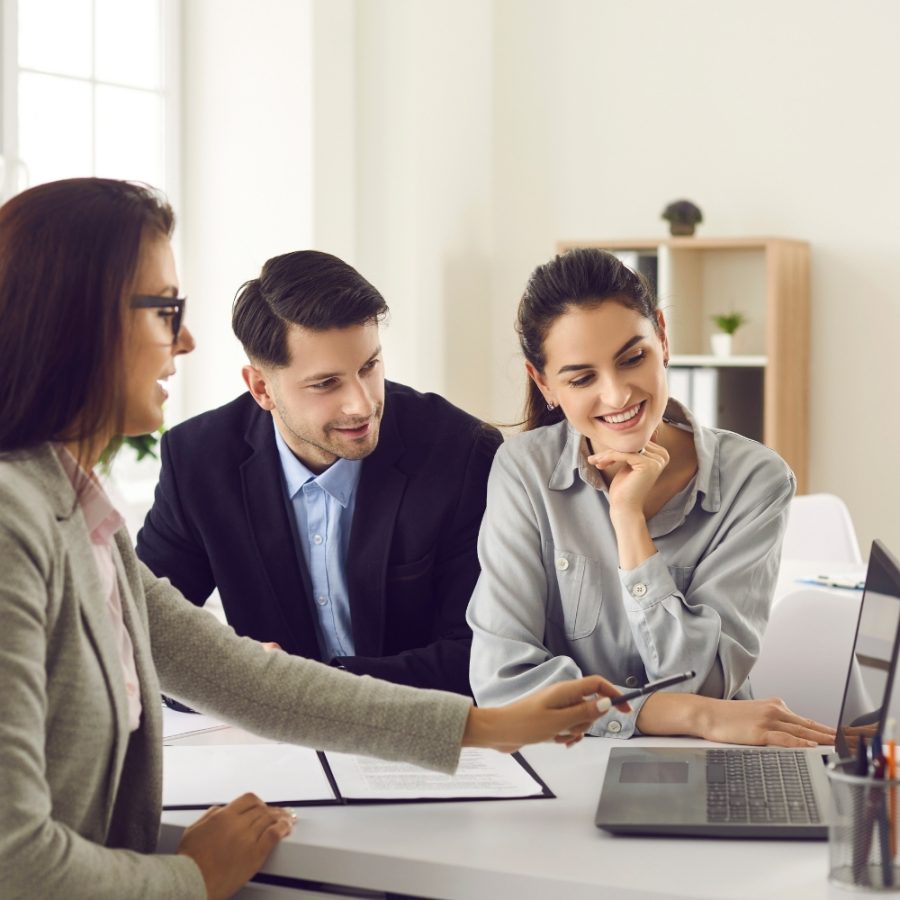 Tres profesionales de negocios sentados a una mesa con un portátil abierto entre ellos.