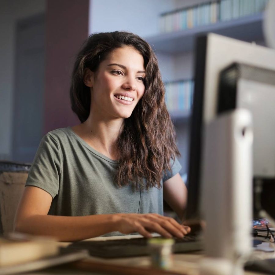 caso de exito Mujer feliz frente a su computadora, disfrutando de su trabajo mientras sonríe.