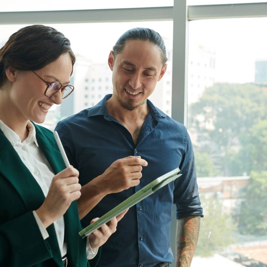 Dos profesionales de negocios frente a una ventana, revisando una tablet juntos en la oficina de Home Vacation Group