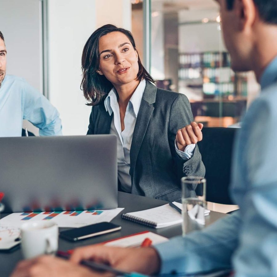 Tres personas de negocios sentadas en una mesa, trabajando juntas en un laptop.