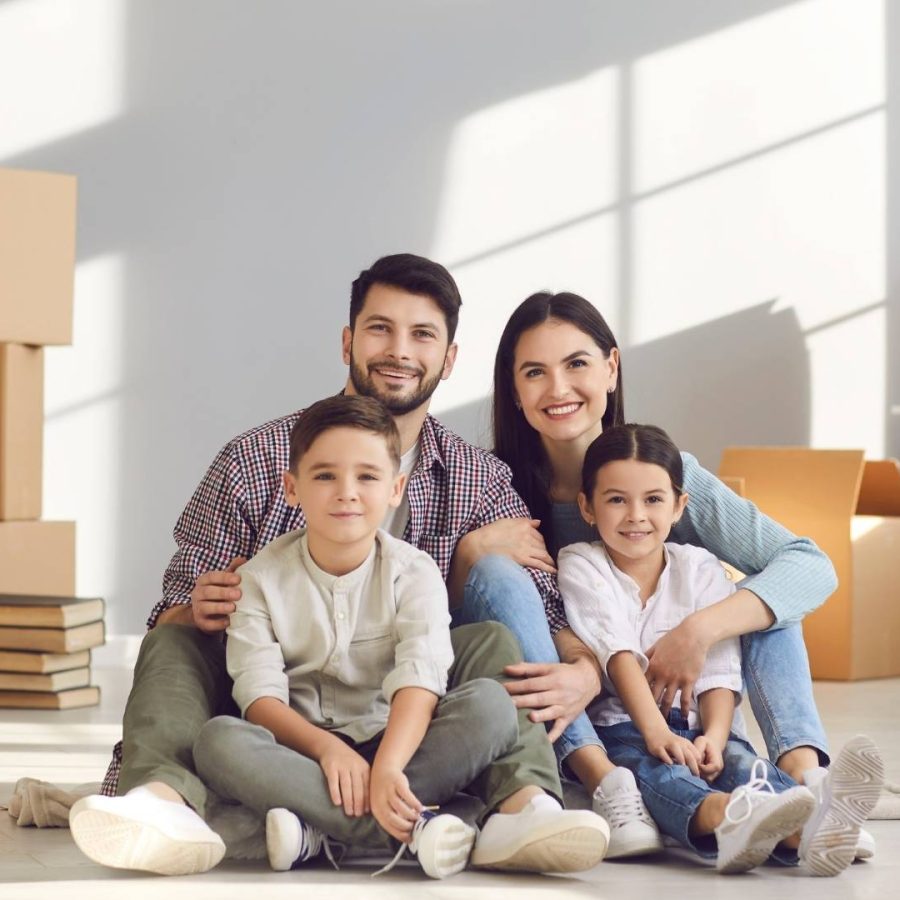 Una familia sentada en el suelo de una habitación vacía rodeada de cajas, disfrutando de su tiempo juntos