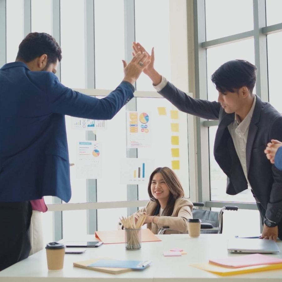 Personas de negocios en una oficina dándose un choque de manos en señal de celebración.