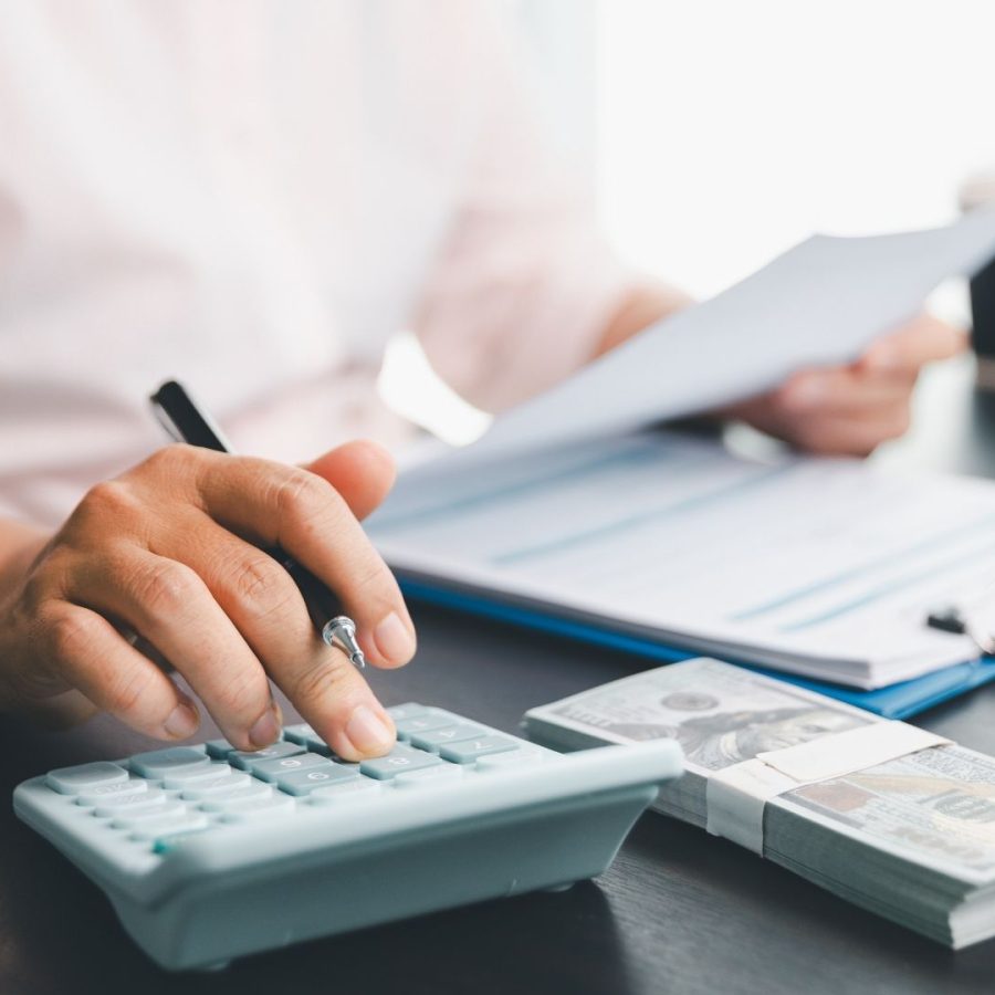 Mano de mujer escribiendo en una calculadora mientras sostiene dinero, evaluando gastos o ingresos.