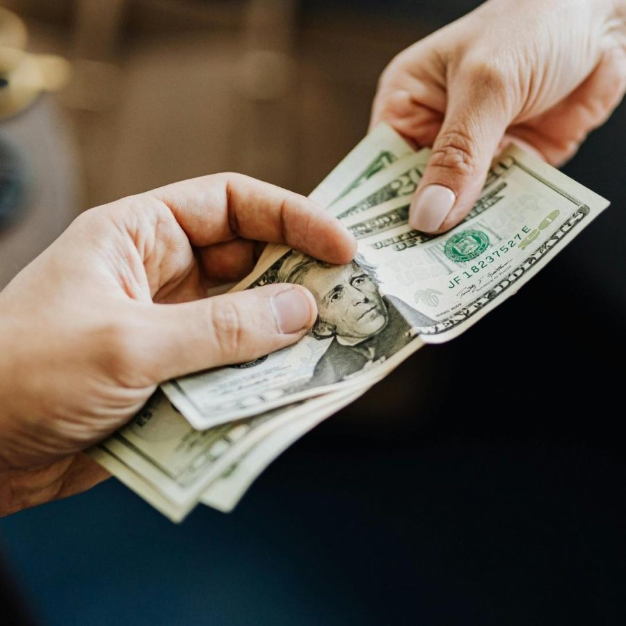Persona entregando dinero en dólares a otra persona.