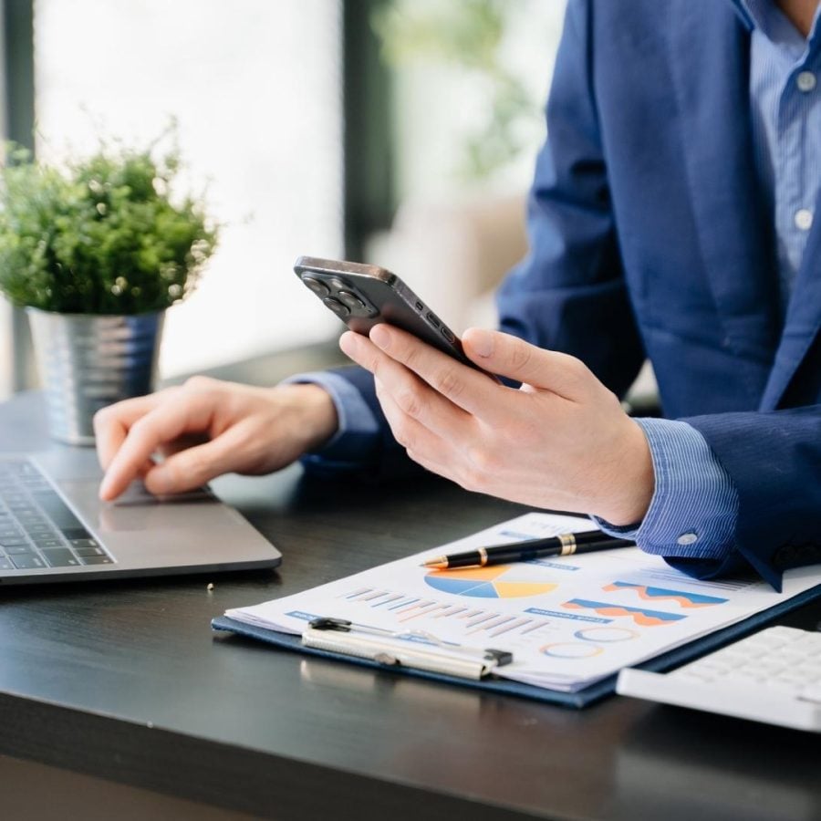 Empresario sentado en su escritorio, usando su smartphone, simbolizando una buena administración en su trabajo diario.