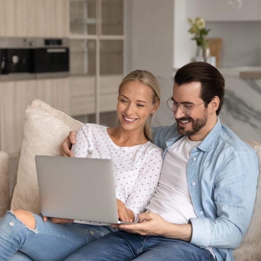 Un hombre y una mujer sentados en un sofá, usando un laptop para buscar información sobre renta.