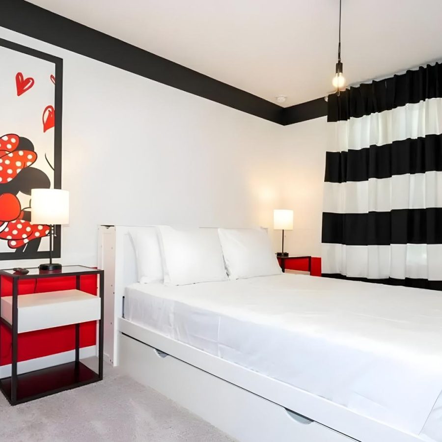 Dormitorio con pared de rayas rojas y blancas y una pintura de Mickey Mouse, reflejando tendencias modernas en decoración.