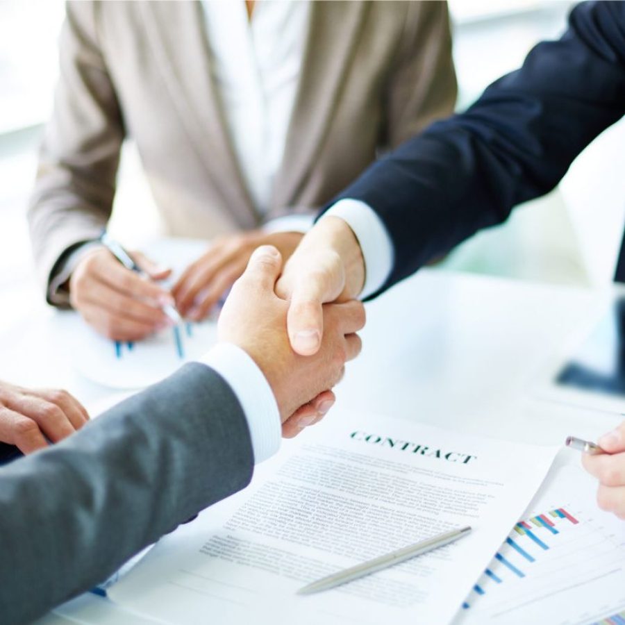 Imagen de socios comerciales estrechándose la mano sobre objetos de trabajo en el lugar de trabajo.