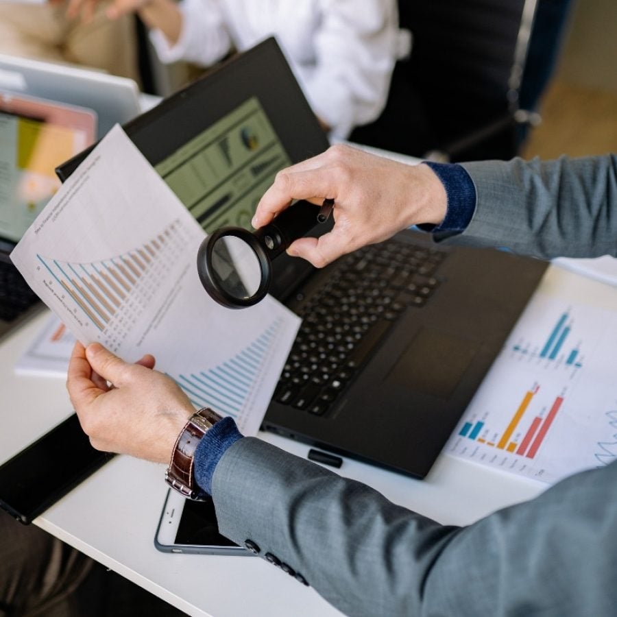 Análisis de gráficos y datos financieros con lupa en laptop, representando un informe trimestral inmobiliario detallado.