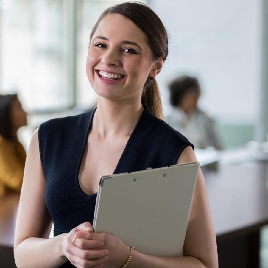 Mujer sonriente sosteniendo una carpeta, mostrando una actitud positiva y amigable.